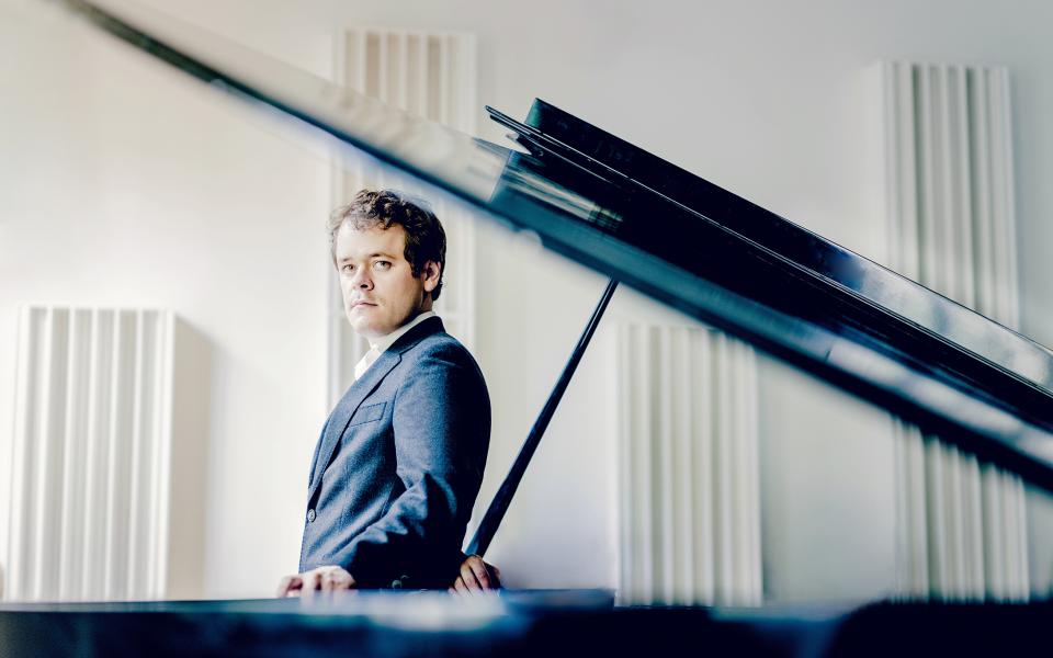 Benjamin Grosvenor standing by a piano