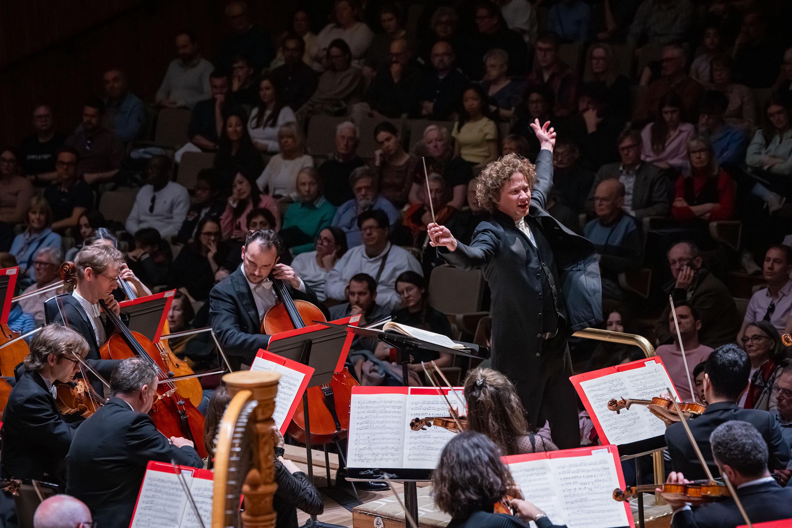 Santtu standing at the front of the orchestra conducting.