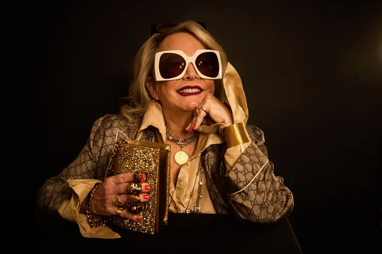 Laura Karpman with sunglasses on smiling at the camera with hand rested on cheek